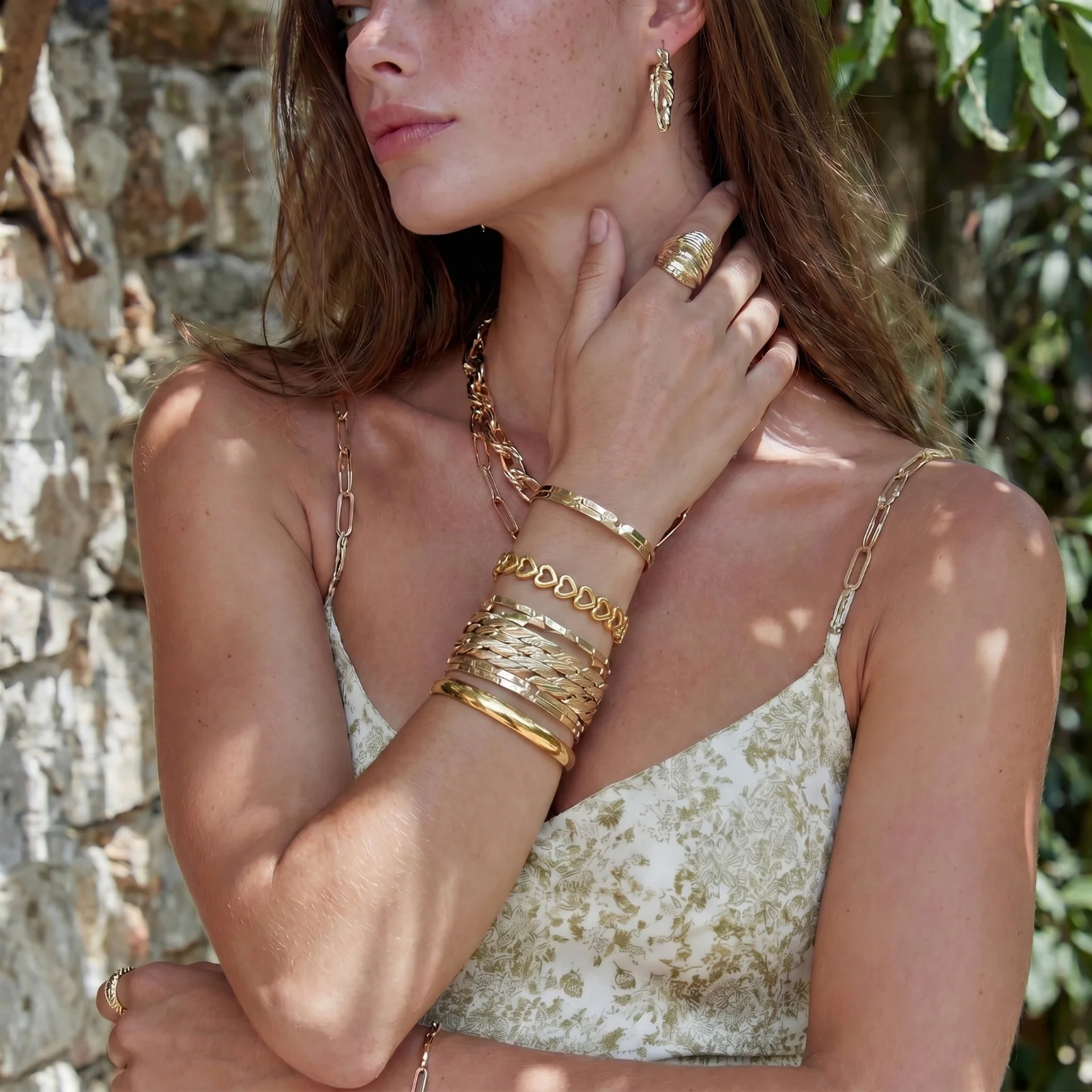 Stacked gold bangles and cuffs on a sunlit wrist