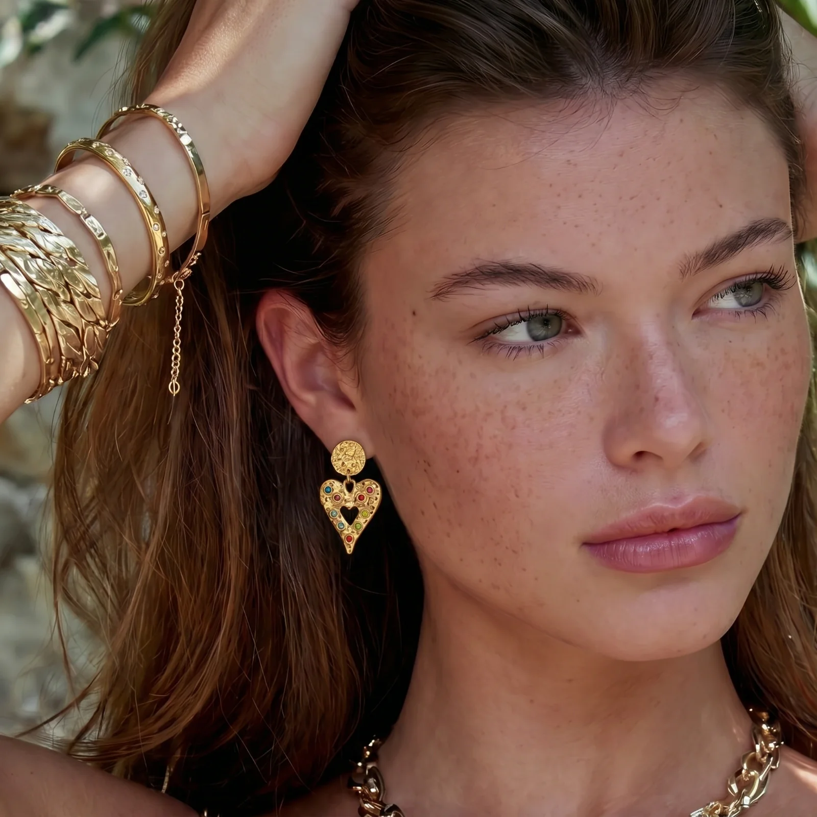 Close-up of stacked gold bracelets and a heart earring